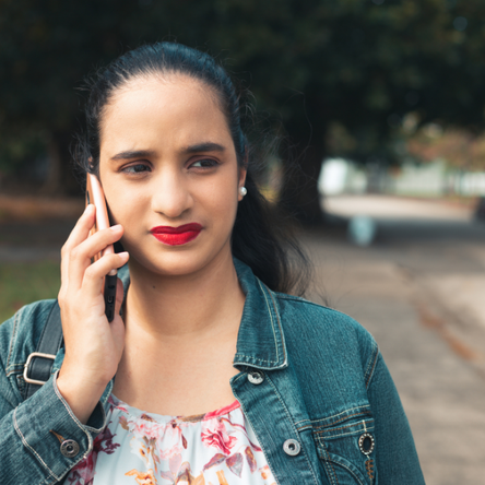 A young woman stands outside. She is talking to someone on her smartphone and is frowning.