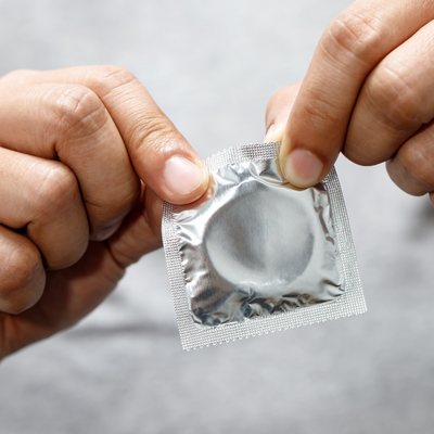 This image shows a man's hands opening a condom. His face isn't visible.