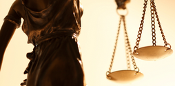 The image shows a photo of the back of a statue of Lady Justice, holding up scales in her right hand.