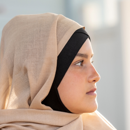 A young woman wearing a beige-coloured headscarf looks off to the side. We see her in profile.