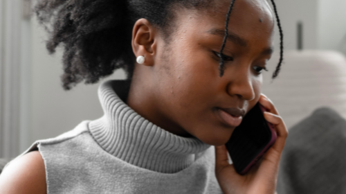 A young woman is on the phone while sat on a sofa.