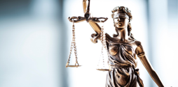 The top of a gold Lady Justice statue against a blurred background.