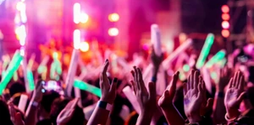 A group of people tightly packed together inside a nightclub but only their hands are in shot. Some of their hands are clapping, others are holding glow sticks.