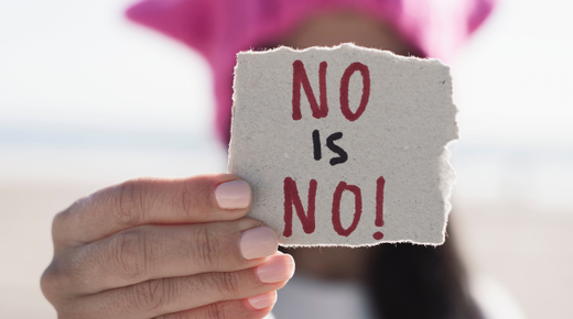 A woman holds up a piece of paper that says 'no is no!' in front of her face.