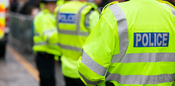 Three policemen stand outside with their backs to the camera. They are all wearing high-vis police jackets and police hats.