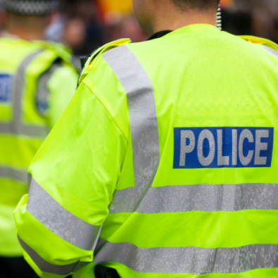 Three policemen stand outside with their backs to the camera. They are all wearing high-vis police jackets and police hats.