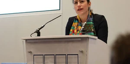 Victoria Atkins, a member of parliament, stands at a podium. She is mid-speech and looks serious.