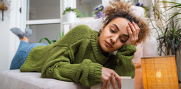 A young woman lies on her front on the sofa. Her head is in her hand and she looks upset upset. Her other hand hangs over the edge of the sofa, holding a journal.