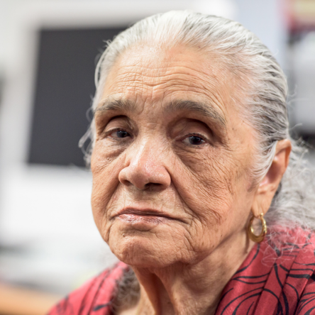 An older woman looks directly at the camera with a sad expression.
