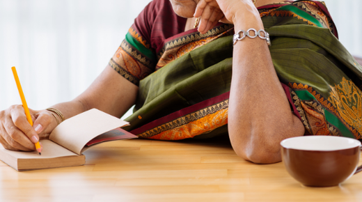 An elderly woman sits at a table and is writing in her journal.