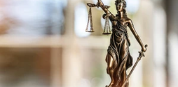 A small bronze statue of Lady Justice against a blurred background.