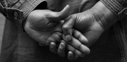 Black and white image of the back of a woman, zoomed in to her hands that she is holding behind her back.
