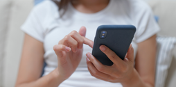 A blurred image of a woman on a phone. Her face is out of shot, and the focus of the camera is on her smart phone, but we can't see what she is doing on it.
